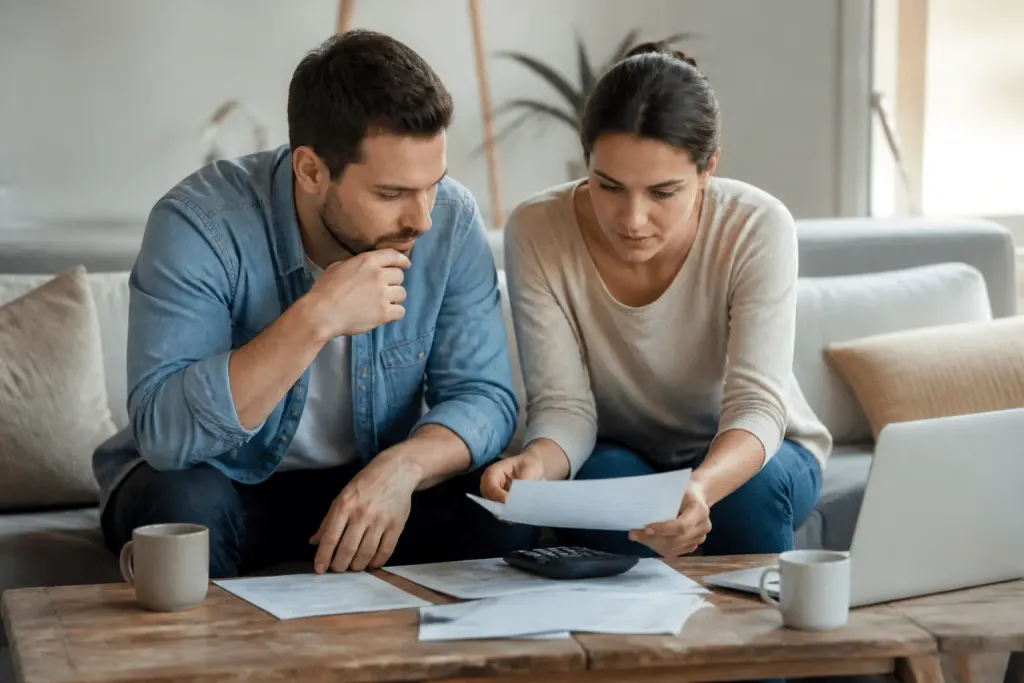 Couple dans salon, documents immobiliers et calculatrice sur table