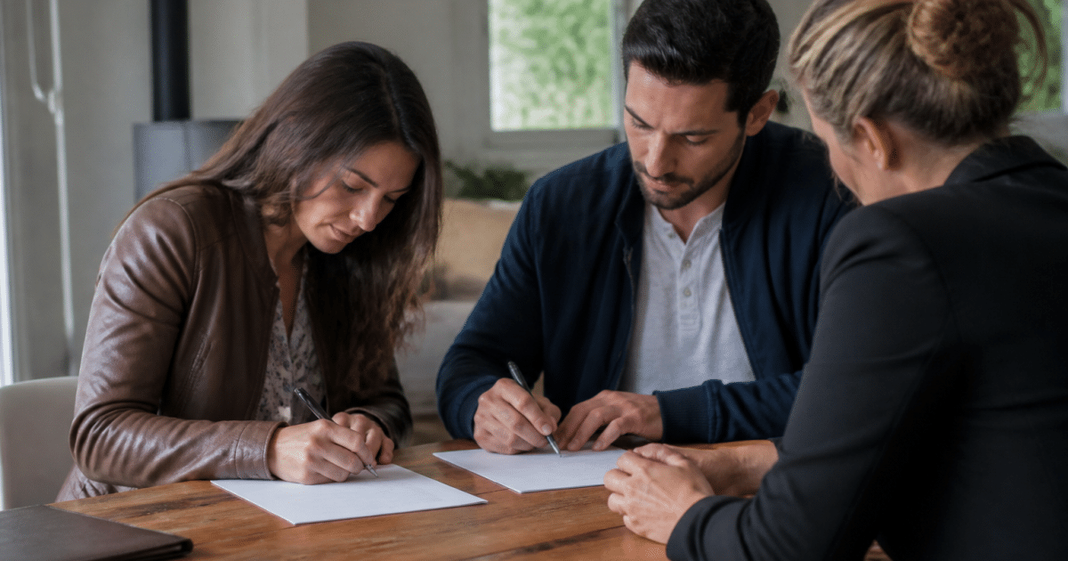 Deux personnes signent documents sur table avec agent immobilier