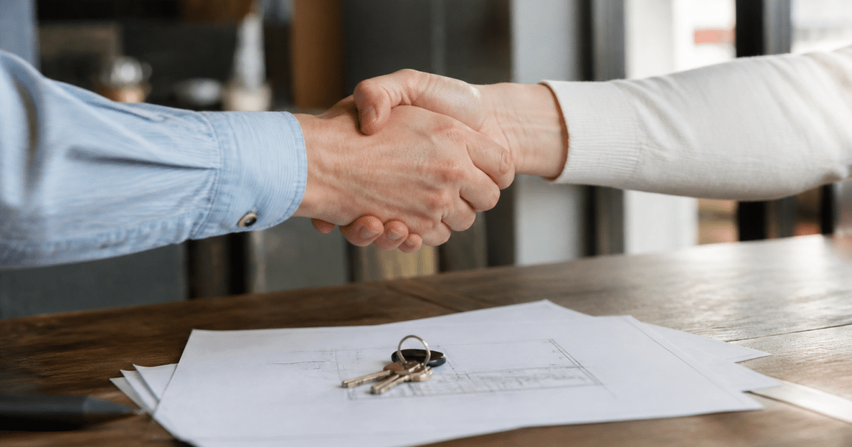 Deux personnes serrant la main devant documents immobiliers